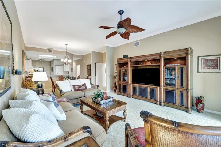 Carpeted living room featuring ornamental molding and ceiling fan with notable chandelier