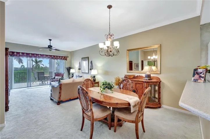 Carpeted dining room with ceiling fan with notable chandelier