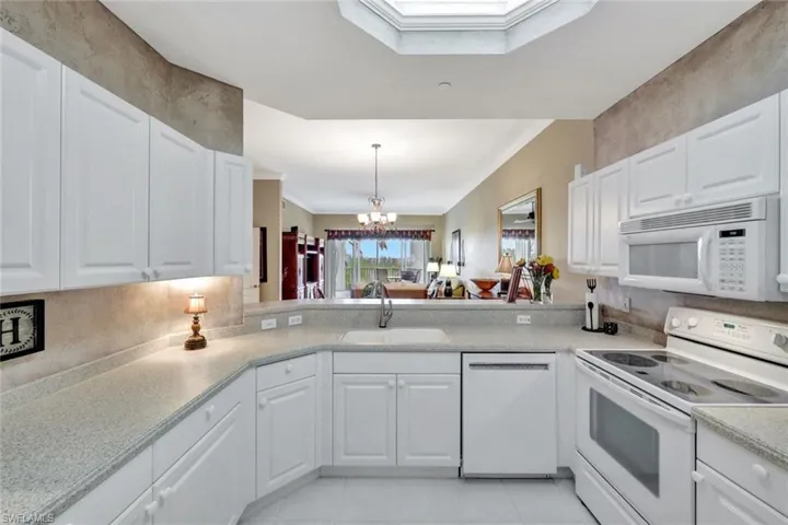 Kitchen featuring an inviting chandelier, sink, white cabinetry, and white appliances
