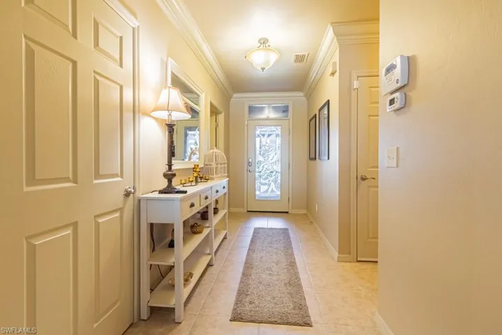 Doorway with light tile patterned floors and crown molding
