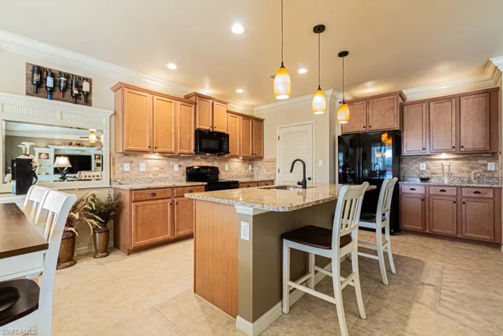 Kitchen with sink, hanging light fixtures, black appliances, light stone countertops, and a center island with sink