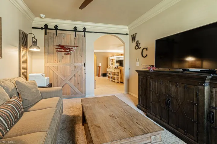 Living room featuring ornamental molding, a barn door, light colored carpet, and ceiling fan