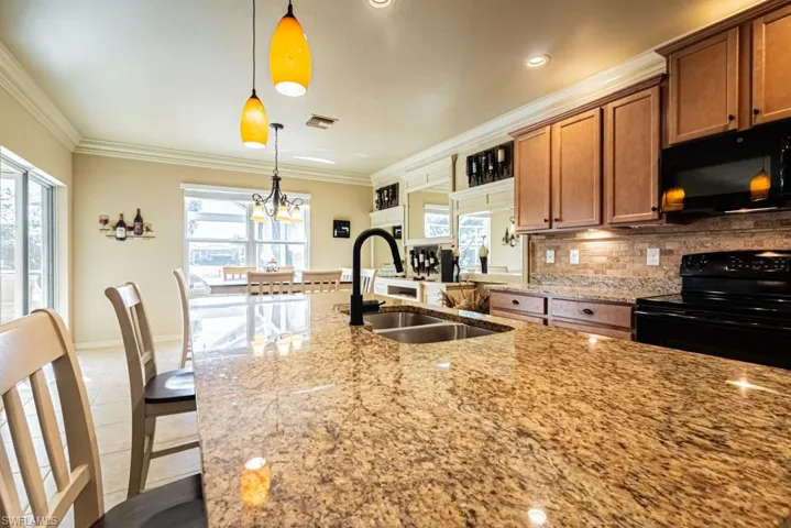 Kitchen featuring sink, black appliances, hanging light fixtures, and light stone countertops