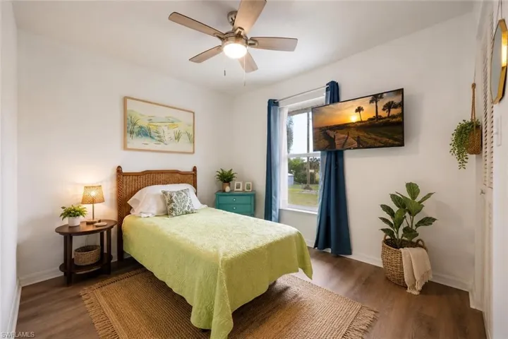 Bedroom featuring a ceiling fan with light fixture, window with blue drapery, and wood-finish flooring