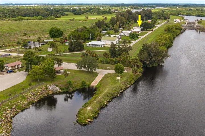 Waterfront property featuring a private boat ramp, rock-lined shore, lush green lawn, and mature trees