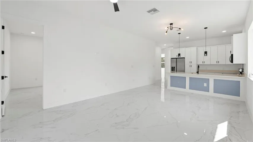 Kitchen with white cabinets, hanging light fixtures, stainless steel refrigerator with ice dispenser, open floor plan, and light marble finish floors