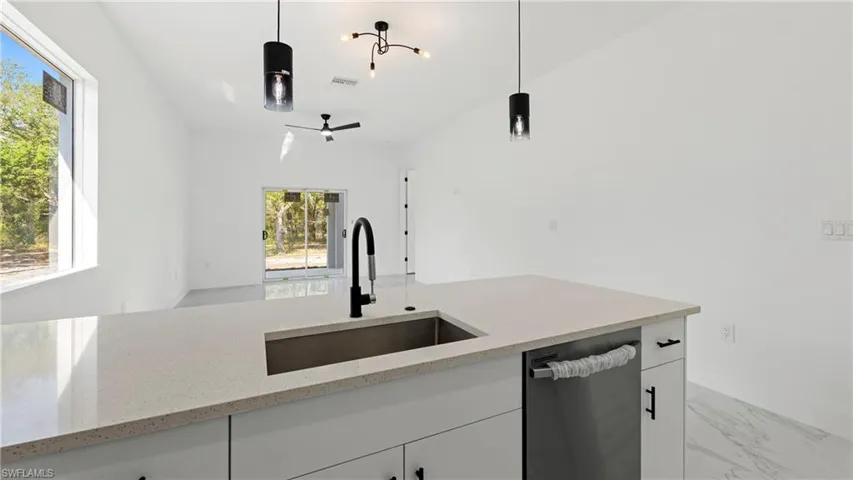 Kitchen featuring white cabinets, dishwasher, light stone counters, and hanging light fixtures