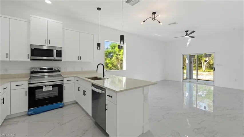 Kitchen with stainless steel appliances, light marble finish flooring, a peninsula, and white cabinetry