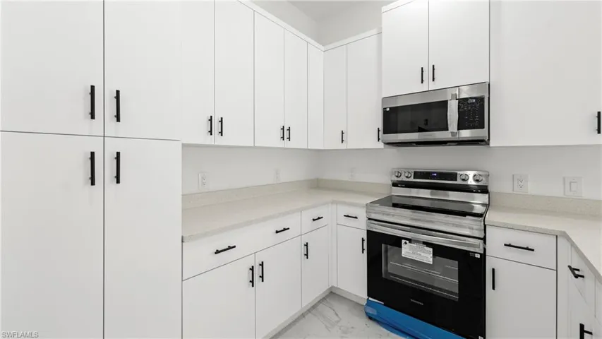 Kitchen featuring stainless steel appliances, white cabinetry, light marble finish floors, and light stone countertops