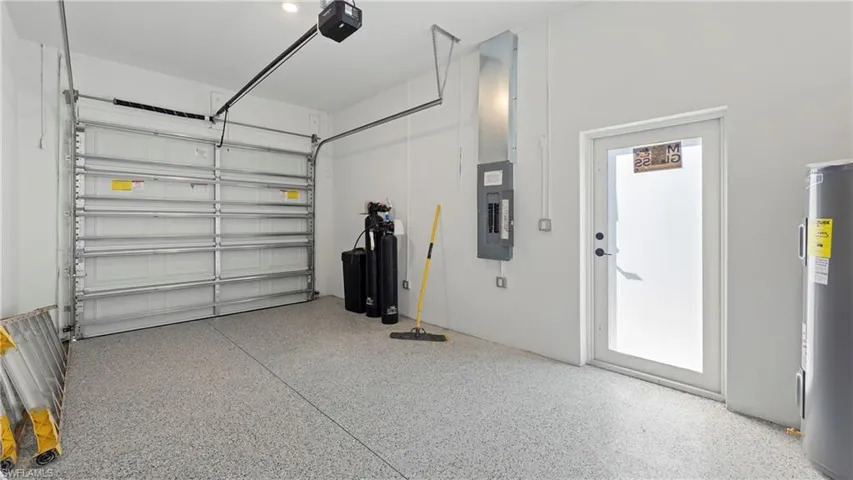 Garage featuring electric water heater, electric panel, and a garage door opener