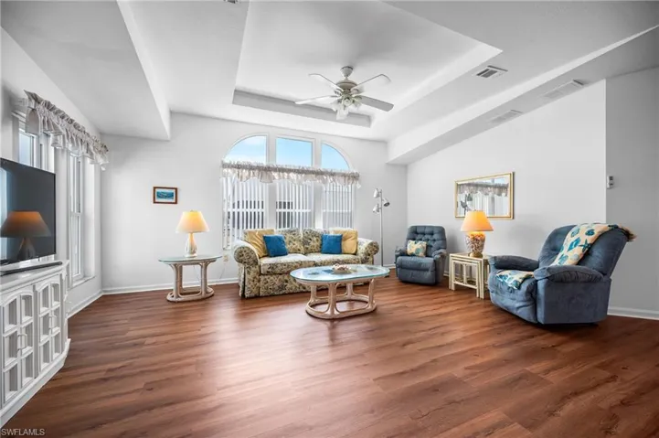 Spacious living area featuring rich wood-finish flooring, a tray ceiling, and an arched window