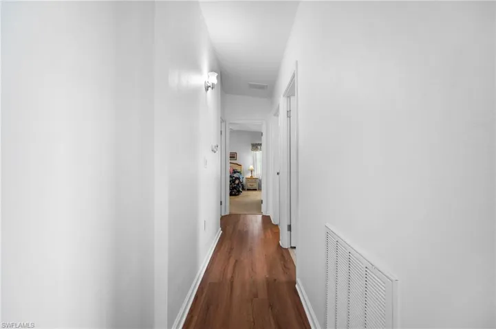 Hallway with wood-finish flooring, white walls, and wall-mounted light fixtures