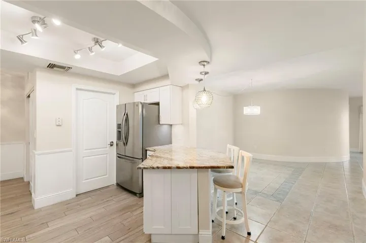 Kitchen featuring white cabinets, a kitchen breakfast bar, light stone countertops, hanging light fixtures, and stainless steel fridge with ice dispenser