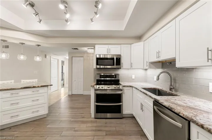 Kitchen featuring appliances with stainless steel finishes, decorative backsplash, white cabinetry, light stone countertops, and hanging light fixtures