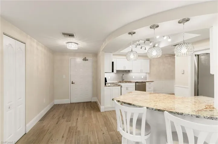 Kitchen with a breakfast bar area, white cabinets, hanging light fixtures, light wood finished floors, and tasteful backsplash