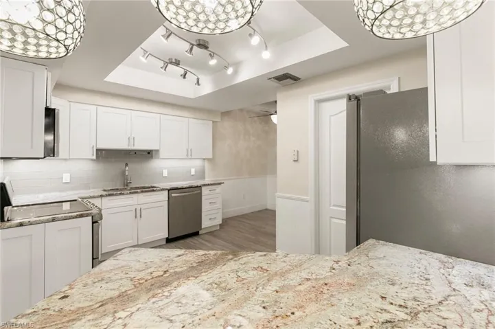 Kitchen featuring white cabinets, a tray ceiling, backsplash, stainless steel appliances, and a wainscoted wall