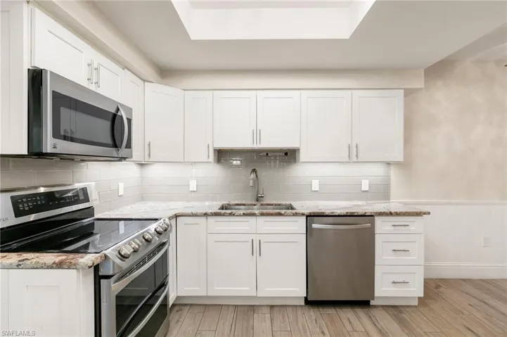 Kitchen featuring appliances with stainless steel finishes, white cabinets, a wainscoted wall, light stone countertops, and light wood-style flooring