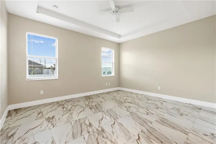 Primary bedroom with a raised ceiling, a ceiling fan, and marble finish floors
