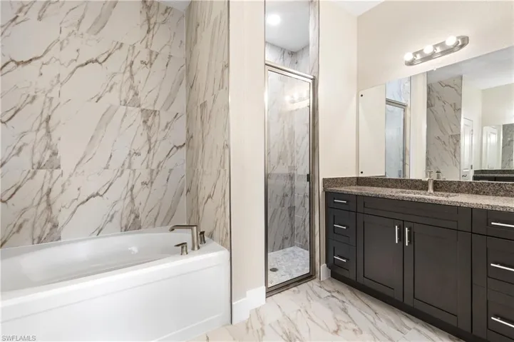Bathroom featuring a garden tub, vanity, a marble finish shower, and light marble finish floors