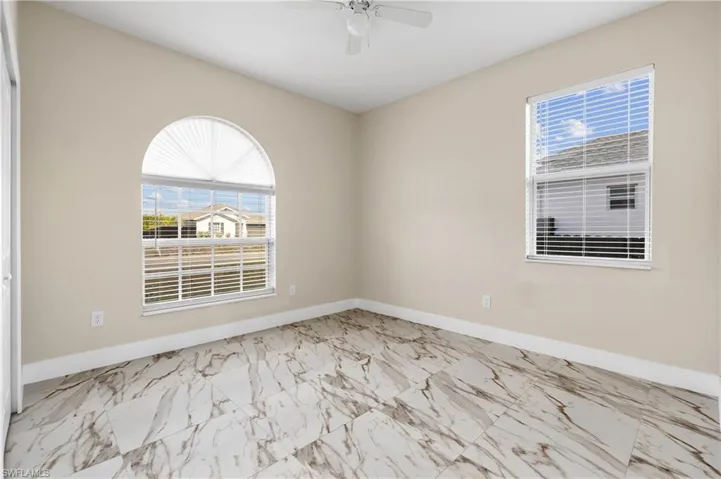 Second bedroom featuring light marble finish floors, plenty of natural light, and ceiling fan
