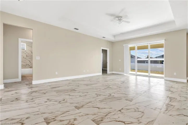 Living with ceiling fan, a raised ceiling, and light marble finish floors