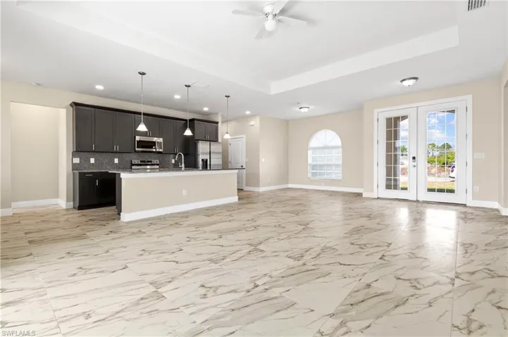 Kitchen with a tray ceiling, french doors, open floor plan, a center island with sink, and decorative light fixtures