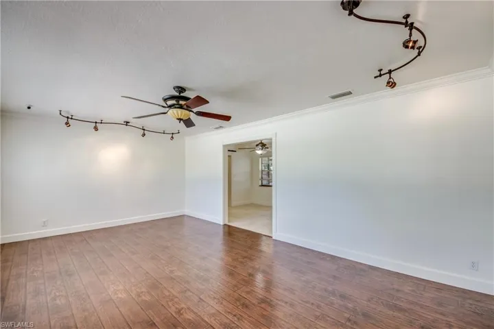 Spare room featuring a ceiling fan, crown molding, rail lighting, hardwood / wood-style flooring, and baseboards
