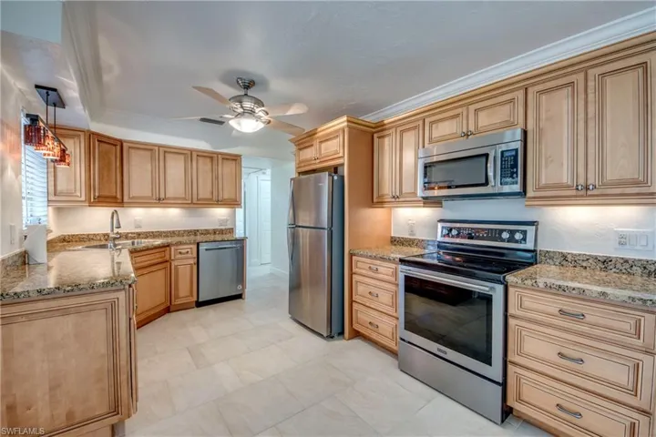 Kitchen featuring stainless steel appliances, a sink, ceiling fan, and light stone counters