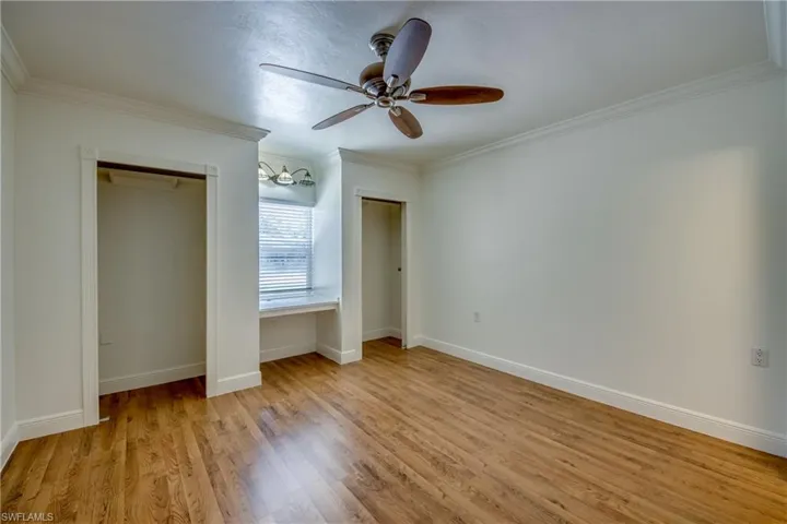 Unfurnished bedroom with multiple closets, crown molding, wood finished floors, baseboards, and ceiling fan