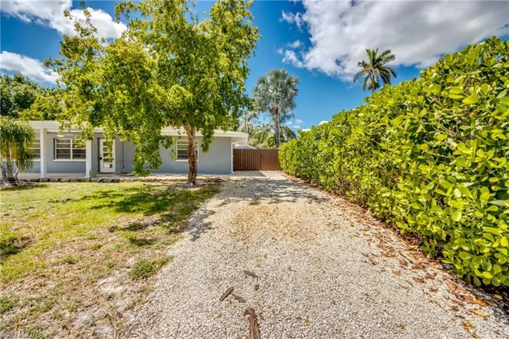 View of property hidden behind natural elements featuring driveway, fence, and stucco siding