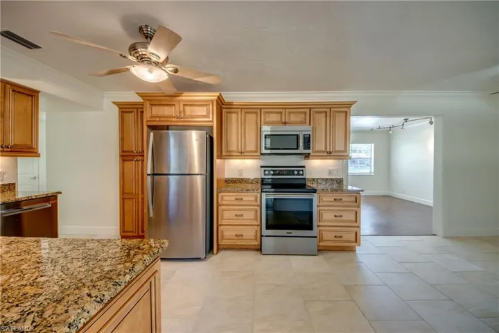 Kitchen with stainless steel appliances, light stone countertops, ceiling fan, ornamental molding, and baseboards