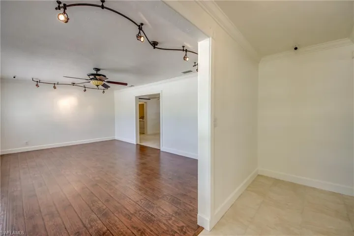 Unfurnished room featuring ornamental molding, ceiling fan, baseboards, wood finished floors, and rail lighting