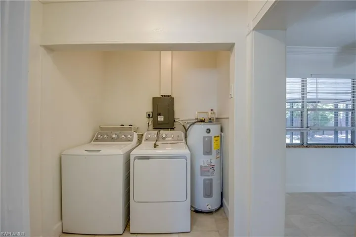 Laundry area with electric water heater, electric panel, washer and dryer, and light tile patterned flooring