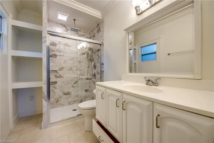 Bathroom featuring a stall shower, ornamental molding, toilet, vanity, and tile patterned flooring