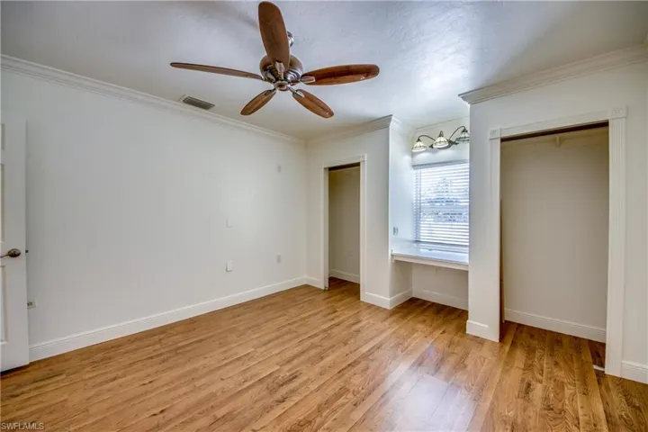 Unfurnished bedroom with multiple closets, light wood finished floors, ornamental molding, baseboards, and ceiling fan