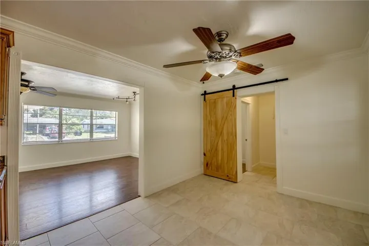 Empty room featuring a barn door, a ceiling fan, crown molding, baseboards, and light tile patterned flooring