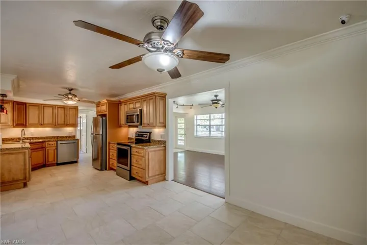 Kitchen featuring stainless steel appliances, ornamental molding, light stone counters, a ceiling fan, and brown cabinetry