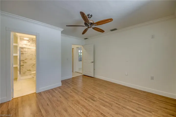 Unfurnished bedroom with ornamental molding, light wood-style flooring, ensuite bathroom, baseboards, and ceiling fan