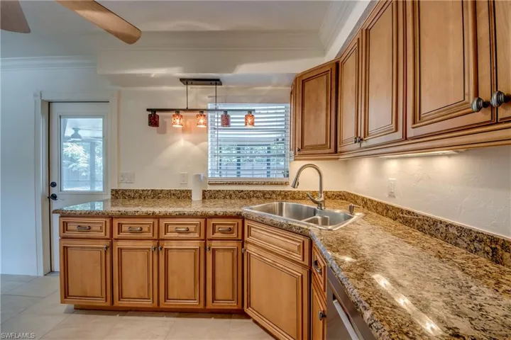 Kitchen featuring a sink, brown cabinetry, crown molding, stone countertops, and decorative light fixtures
