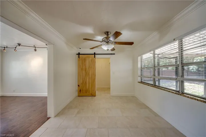 Unfurnished room featuring crown molding, ceiling fan, a barn door, and baseboards