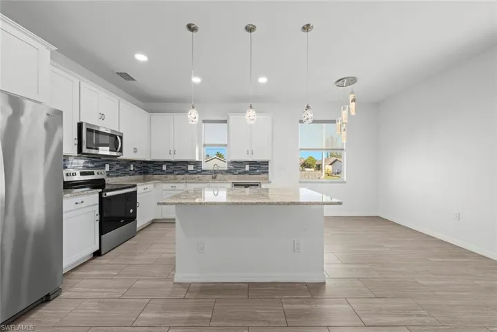 Kitchen featuring white cabinetry, stainless steel appliances, hanging light fixtures, and a kitchen island