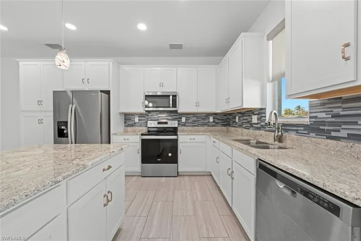 Kitchen with appliances with stainless steel finishes, sink, hanging light fixtures, and white cabinets