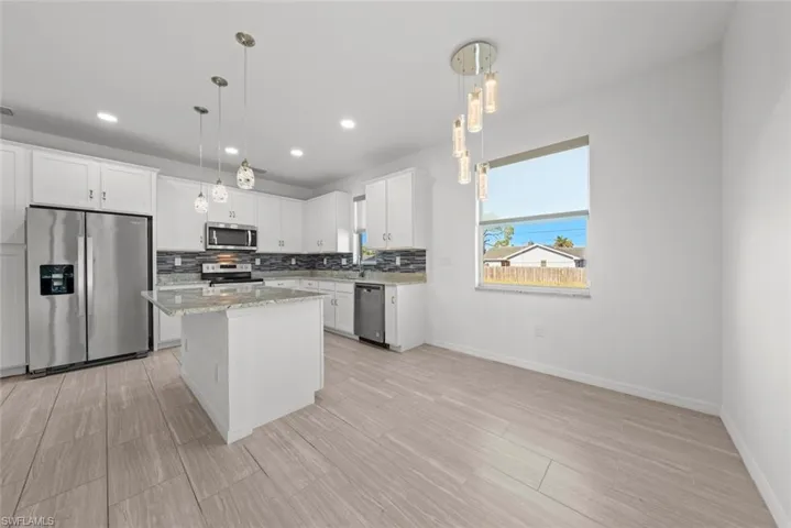 Kitchen with stainless steel appliances, a kitchen island, hanging light fixtures, and white cabinets