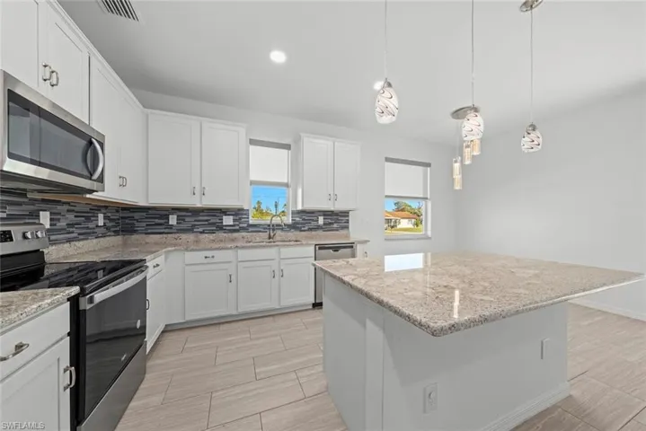 Kitchen with white cabinetry, decorative light fixtures, stainless steel appliances, and a kitchen island