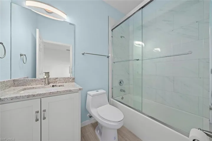 Full bathroom with vanity, combined bath / shower with glass door, wood-type flooring, and toilet