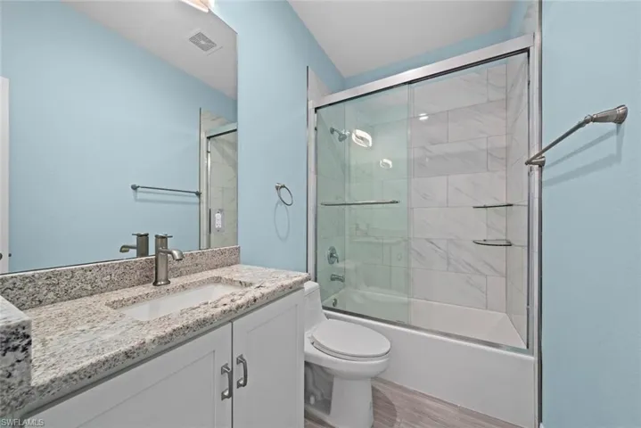 Full bathroom with vanity, hardwood / wood-style flooring, enclosed tub / shower combo, and toilet