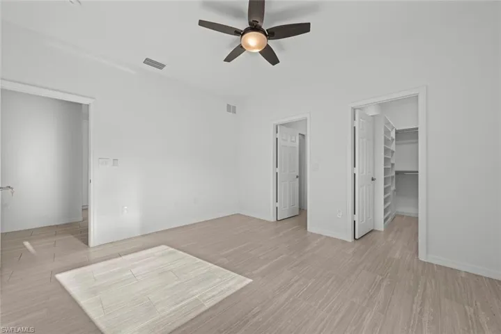 Unfurnished bedroom featuring ceiling fan, a spacious closet, a closet, and light hardwood / wood-style flooring