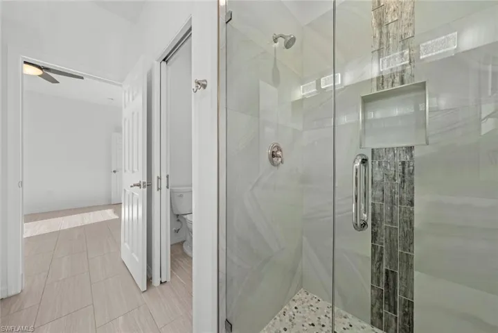 Bathroom with ceiling fan, a shower with shower door, and toilet
