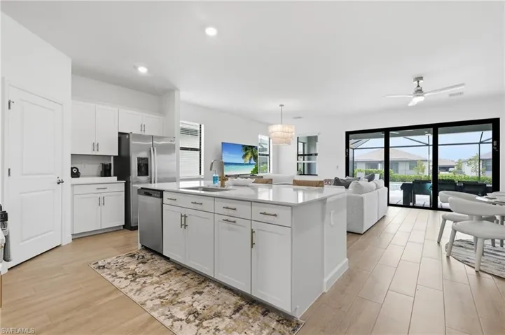 Open-concept living space featuring a central kitchen island with a white countertop, modern white cabinetry, and stainless steel appliances