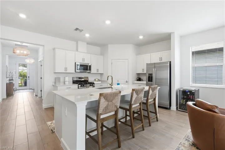 Modern kitchen featuring a large central island with seating, white shaker cabinetry, stainless steel appliances, and sleek countertops